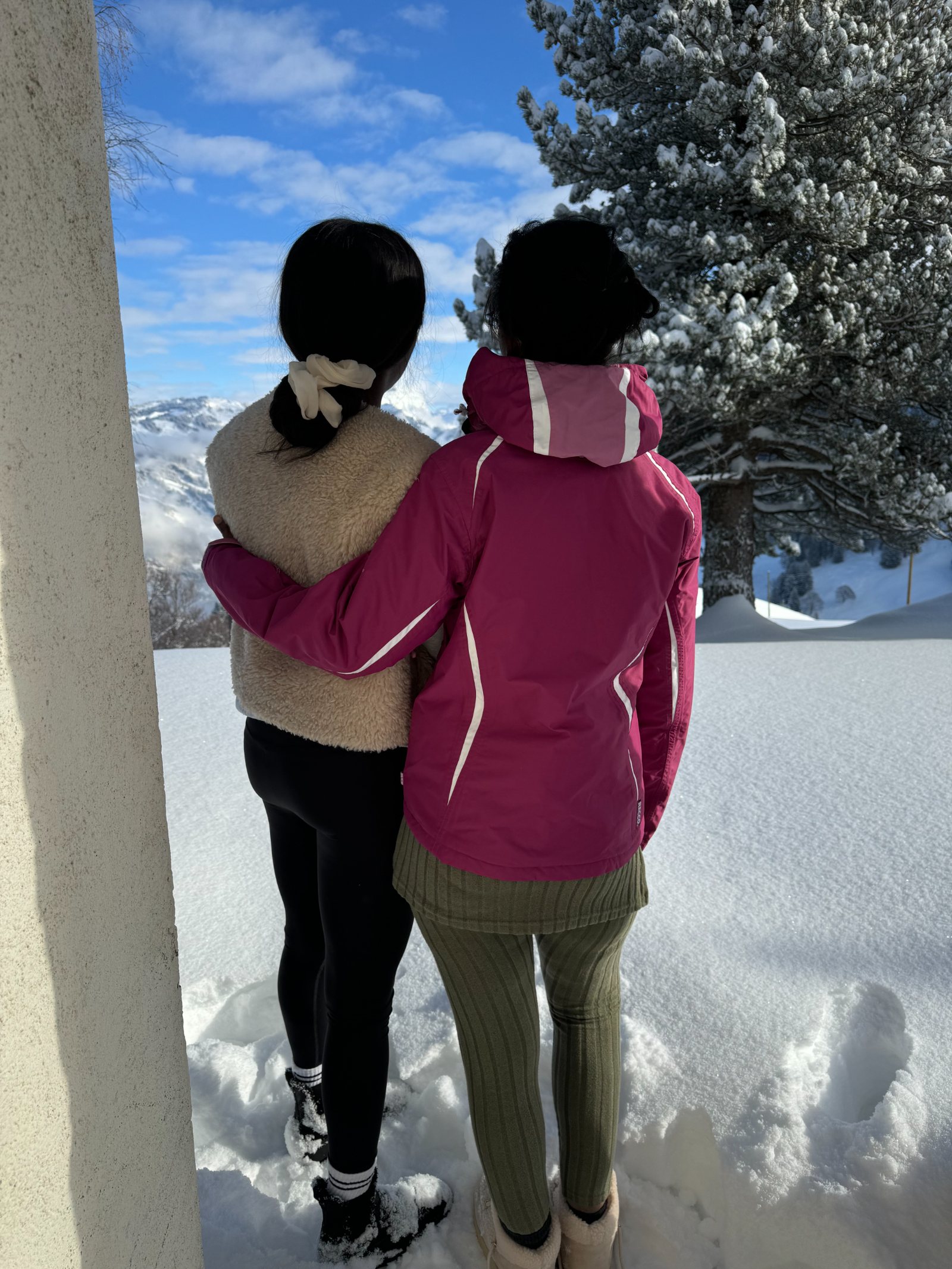 Two women seen from behind in a doorway, arm in arm, looking out at the snow