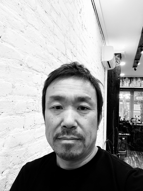 Black and white portrait of a man against a textured white brick wall.