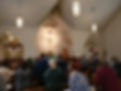 Image from behind of church worshipers standing in the sanctuary, with altar and large cross on the wall at front
