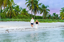 A couple holdings hands in walking along the shore of Smathers Beach with palm trees and dune grasses in the background
