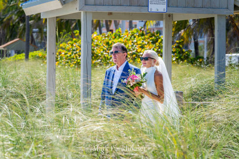 A bride in a white CasaBlanca Bridal dress is standing at an entrance to Smathers Beach waiting for her wedding to start