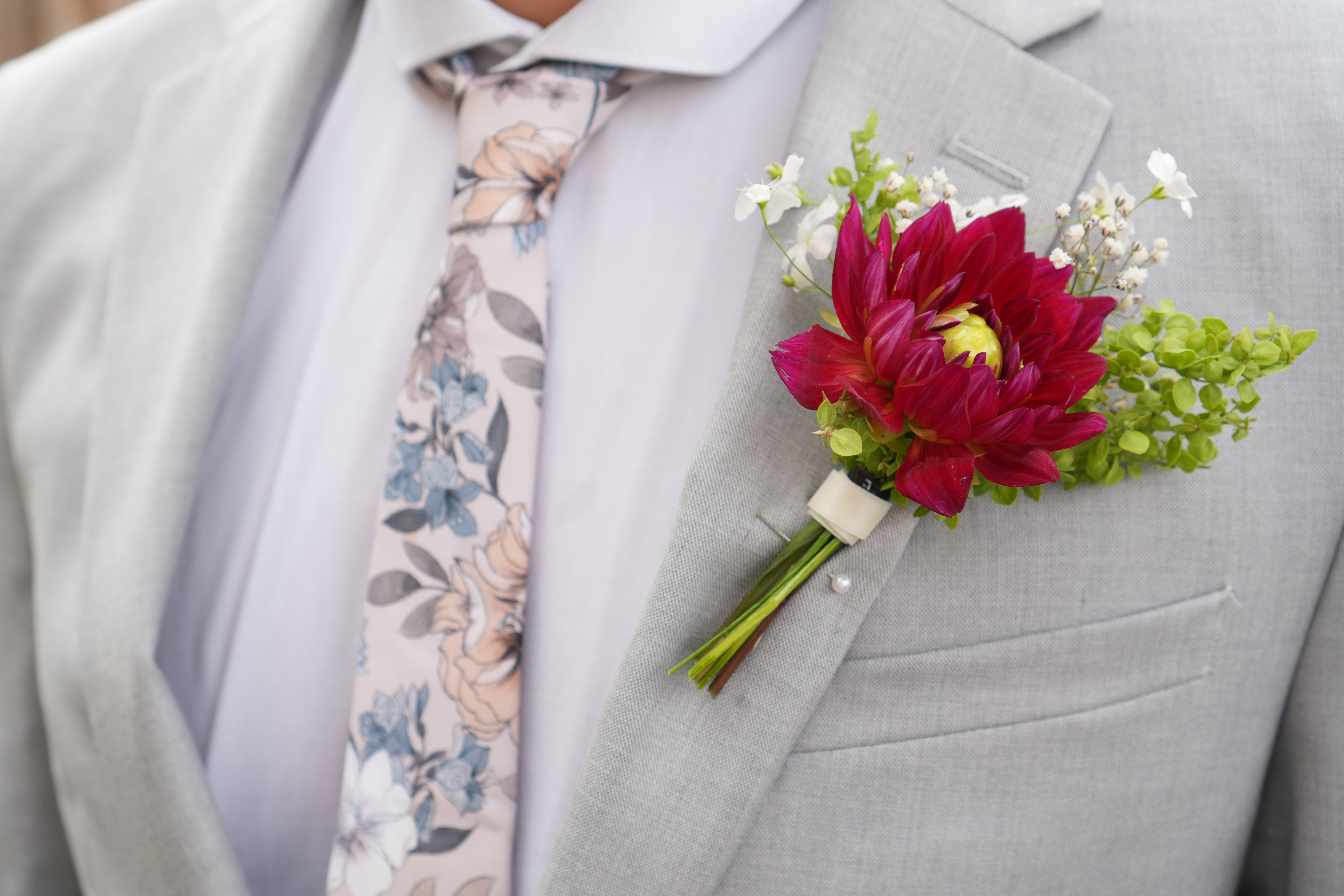 A close-up of a groom's buttonhole featuring a deep red dahlia
