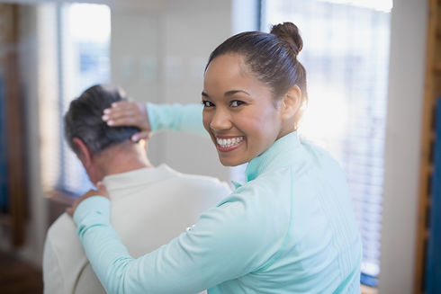 Rear view of portrait of smiling female therapist giving neck massaging to senior male pat...ard.jpg