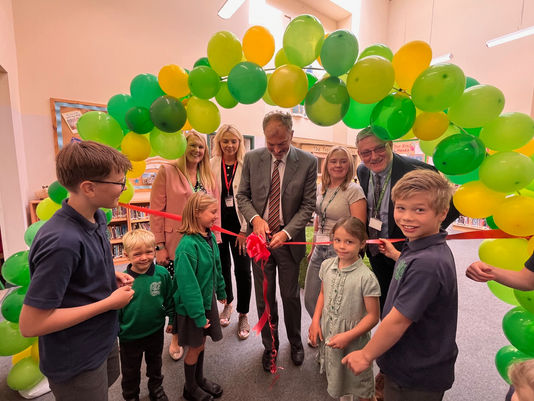 cutting a ribbon under a balloon arch
