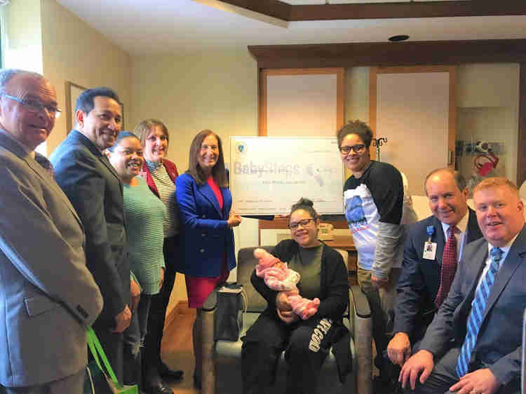 Treasurer Goldberg standing with a group people, including parents and a newborn baby, while holding a large BabySteps check