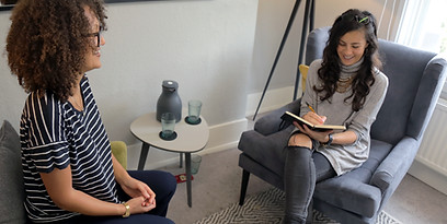 Kelly Mulhall sitting opposite a client in London with her notebook, discussing her clients symptoms. They are both smiling.