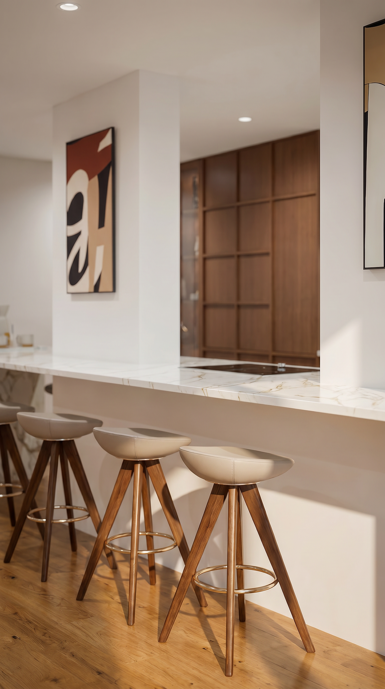 Render fotorrealista de uma cozinha moderna e elegante, destacando uma ilha central com balcão em mármore branco com veios subtis. Três bancos altos de design sofisticado, com assentos estofados em pele clara e pernas de madeira escura com detalhes em metal dourado, estão alinhados ao longo do balcão. Ao fundo, uma parede branca exibe uma obra de arte abstrata em tons terra e preto, e revela um vislumbre de armários de madeira escura no que parece ser a área de despensa ou um bar. A luz natural cria um ambiente acolhedor, com sombras projetadas na parede e no chão de madeira clara. O foco está nos detalhes dos materiais e na composição equilibrada do espaço.