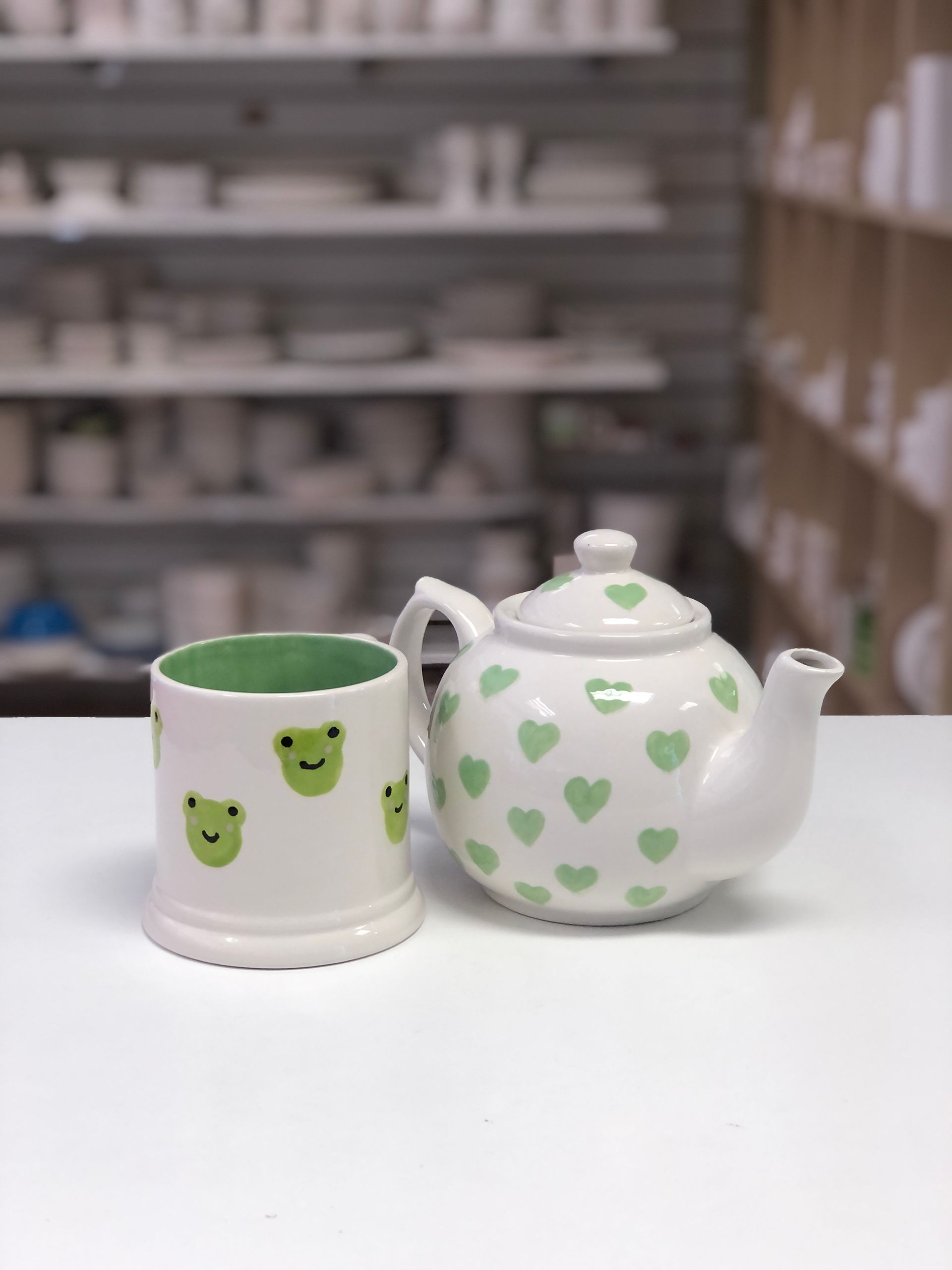 Frogs painted on a mug and green hearts painted on a pottery teapot