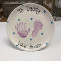 A coupe plate with a baby's hand and foot print on and the wording 'To Daddy , Love Arwen'.