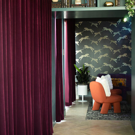 Maximalist amenities area, with patterned wallpaper and colorful accents. Featuring custom-made red velvet drapery.