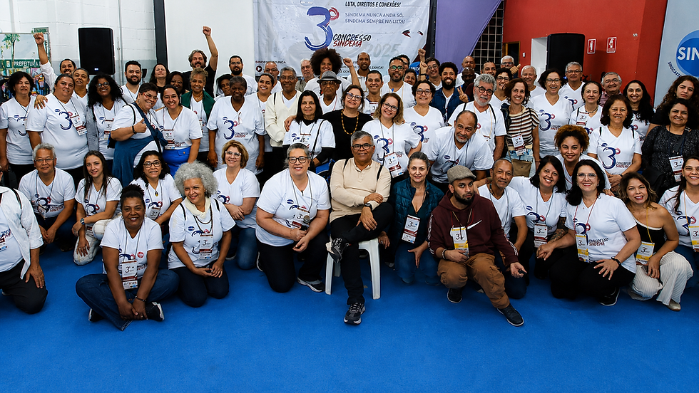 Grande grupo sorri e posa no 3º Congresso Sindema, em salão com piso azul e banner ao fundo.