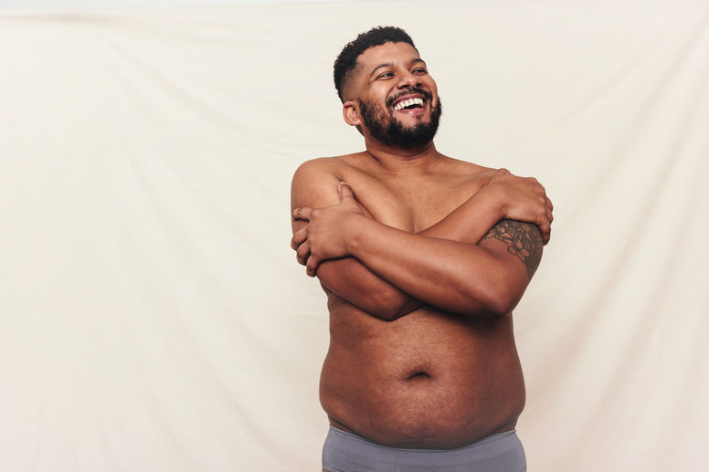 Man with pot belly embracing his natural body. Happy young man laughing cheerfully while s