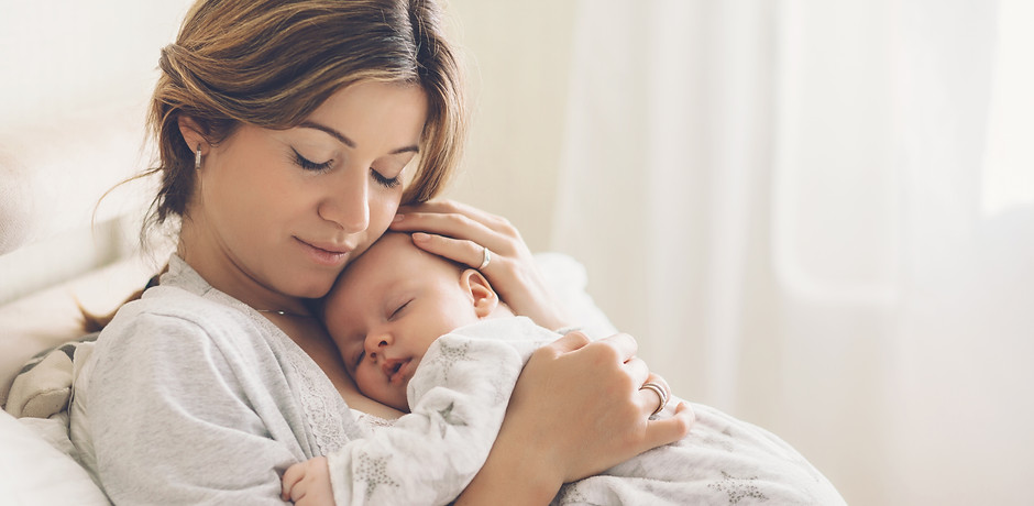 Loving mom carying of her newborn baby at home. Bright portrait of happy mum holding sleep