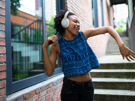 Jovem curtindo a música em seu fone JBL Tune enquanto dança ao ar livre, cheia de energia e alegria. (Imagem divulgação JBL)