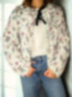 Lightweight cream quilted jacket with floral pattern, long sleeves, and feminine tie-front detailing.