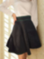 High-waisted black skater skirt with green embroidered detailing at the waistband and hem.