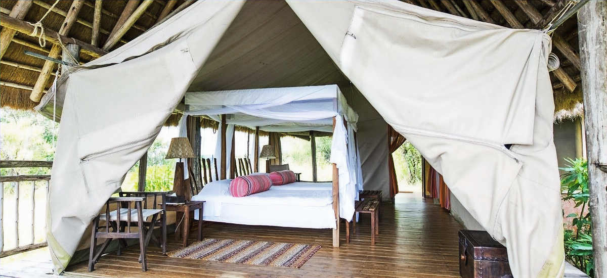 This image shows a tented suite at Mihingo Lodge, featuring a four-poster bed with mosquito netting on a wooden platform.