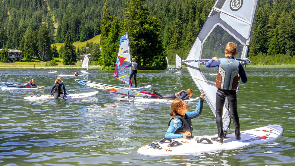 This image shows a scene of windsurfing and paddleboarding on Lake Heidsee in Lenzerheide, Switzerland.