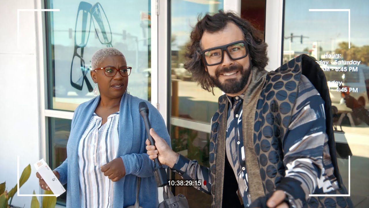 LaKesha Glover in red glasses on set for Stanton Optical, beside an interviewer holding a microphone