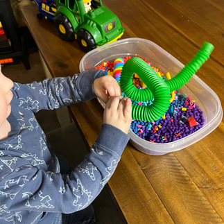 A sensory bin using a clear tub with colorful chickpeas, fidget toys, plastic tweezers, colorful blocks and alphabet letters