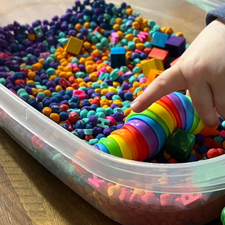 A sensory bin using a clear tub with colorful chickpeas, fidget toys, plastic tweezers, colorful blocks and alphabet letters