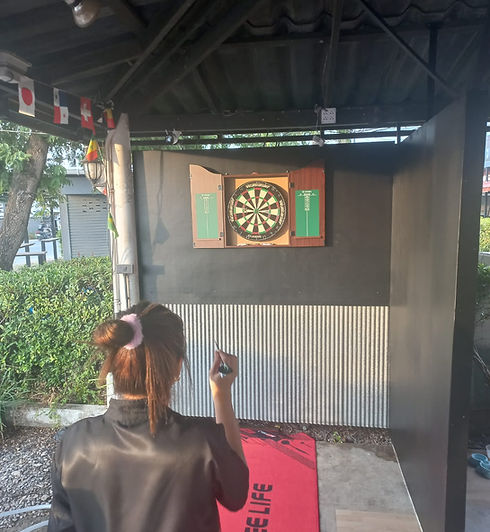 A woman prepares to throw a dart at a vibrant outdoor dartboard setup, standing on a bright red CYEE LIFE mat under a canopy