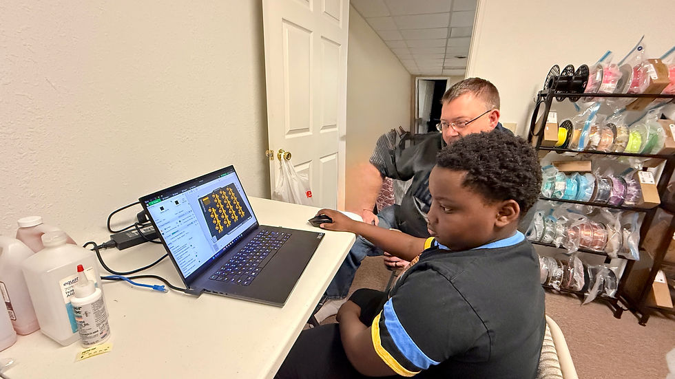 Boy and his dad at a desk, engaged with a laptop displaying a software interface. Shelves with colorful spools in the background.