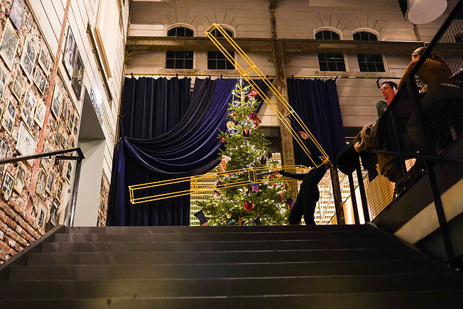 A female performer on top of the stairs, gracefully moving a long, yellow construction that extends her arms, almost touching the ceiling of a movie theater.