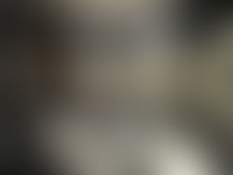 Modern bathroom with black fixtures, glass shower, round LED mirror, and wooden shelves. Dark walls create a sleek, minimalist look.