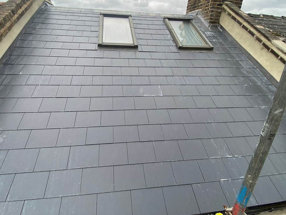 Gray slate roof with two skylights, bordered by brick chimney. Overcast sky in background. Scaffolding visible on right side.