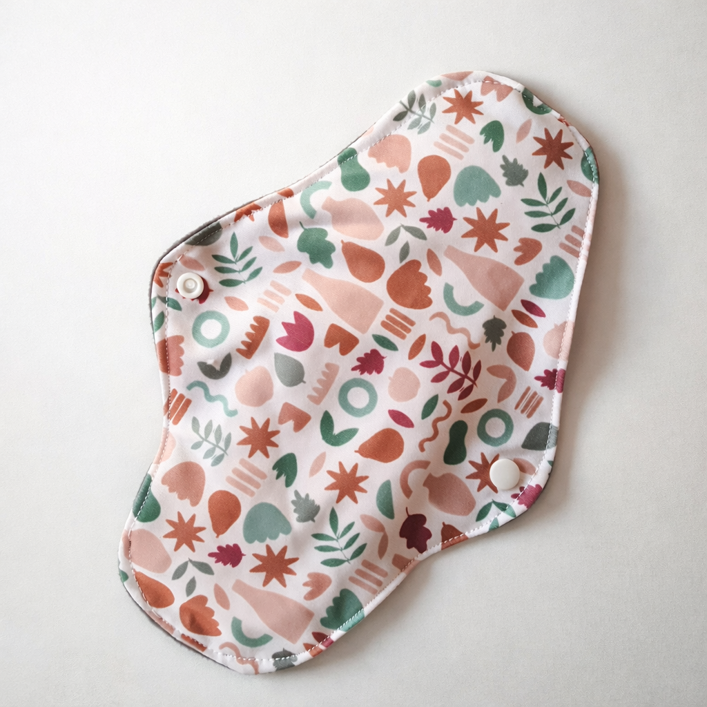 Protection hygiénique lavable en tissu, motif végétal multicolore, avec boutons-pression, posée sur fond clair.