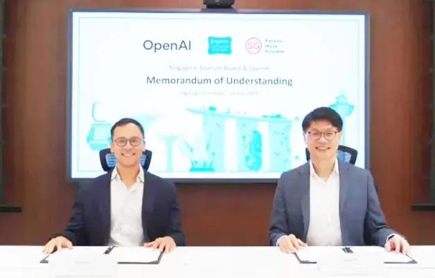 Two people sit at a table signing documents. A screen displays "OpenAI", "Singapore Tourism Board", and "Memorandum of Understanding".