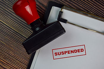 A red stamp on a clipboard marks a paper with "SUSPENDED" in bold red letters against a wooden background.