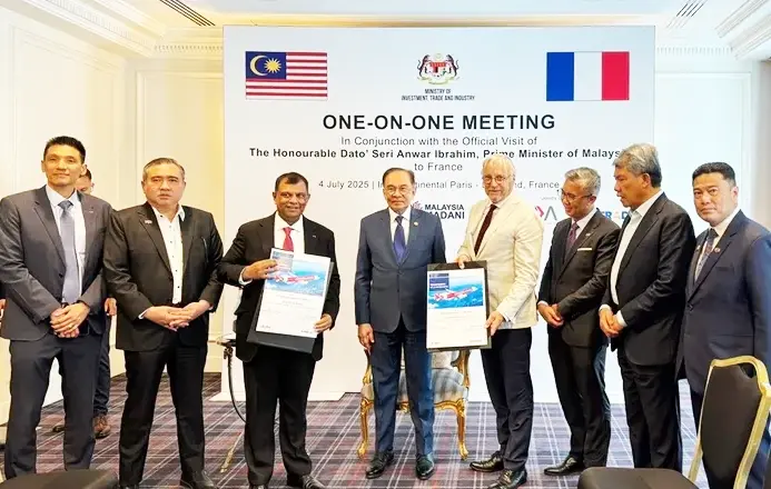 Men in suits at a meeting, holding framed documents. Background shows flags of Malaysia and France, and text about a one-on-one meeting.