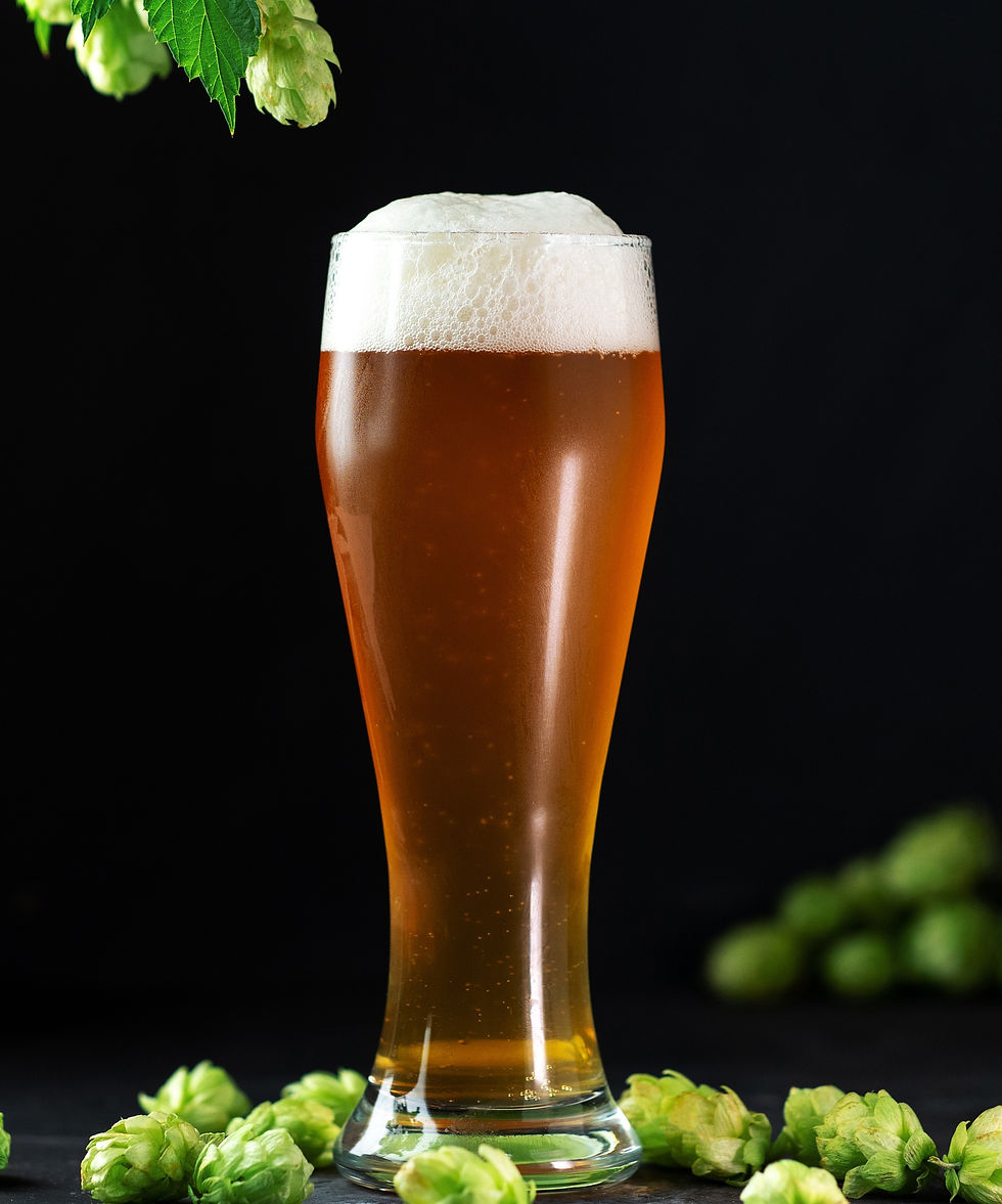 Tall glass of amber beer with foam on top, surrounded by green hops, set against a dark background, conveying a fresh mood.