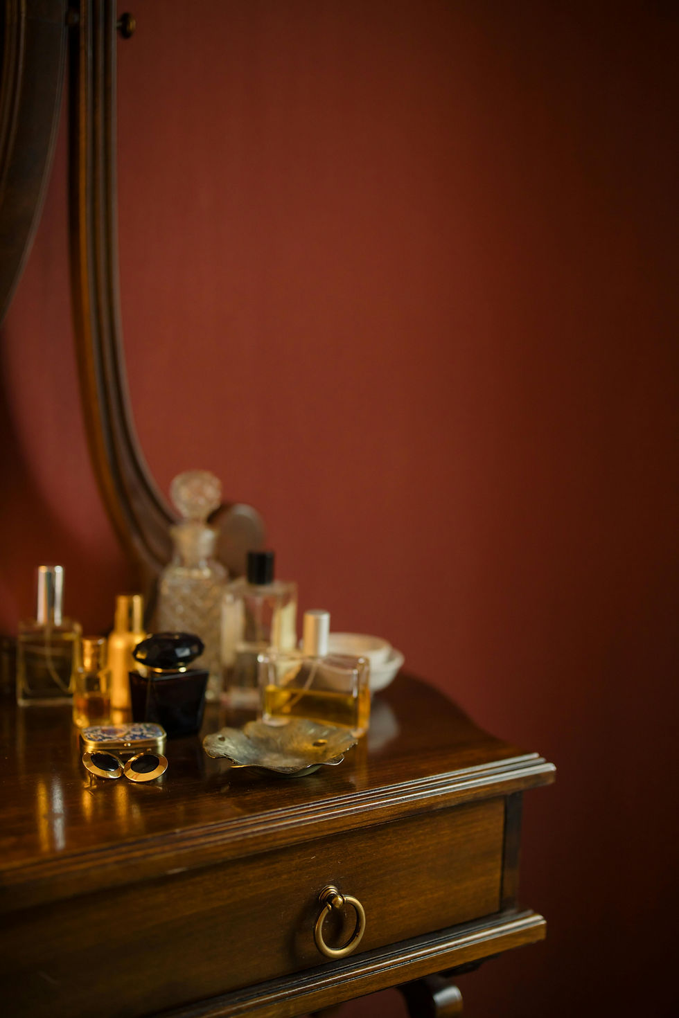 Nine perfume bottles on a wooden dresser with a small mirror against a burgundy wall.