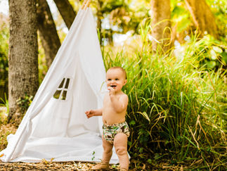 baby in a cloth diaper near tent in a forest