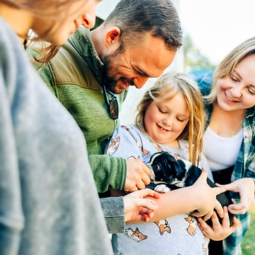 Family of four holding a black and white Boston terrier puppy