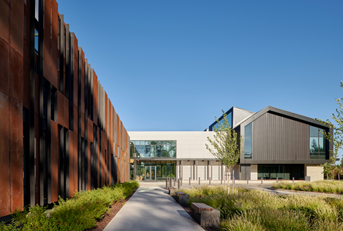 The Outside of a credit union with landscaping and mixed materials used. Wood, metal, and glass.