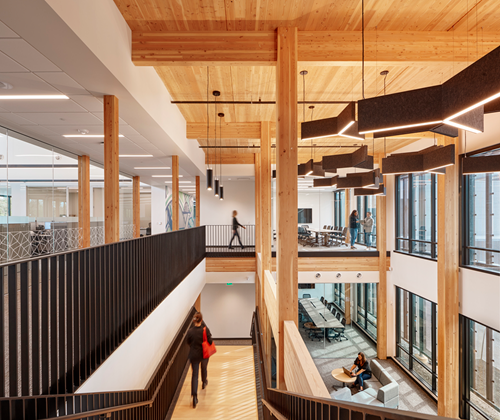 An overview mass timber inside the credit union building of the staircases, the wooden mass timber beams and CLT panels on the ceilings. You can see the lobby and the 2nd floor at the same time.