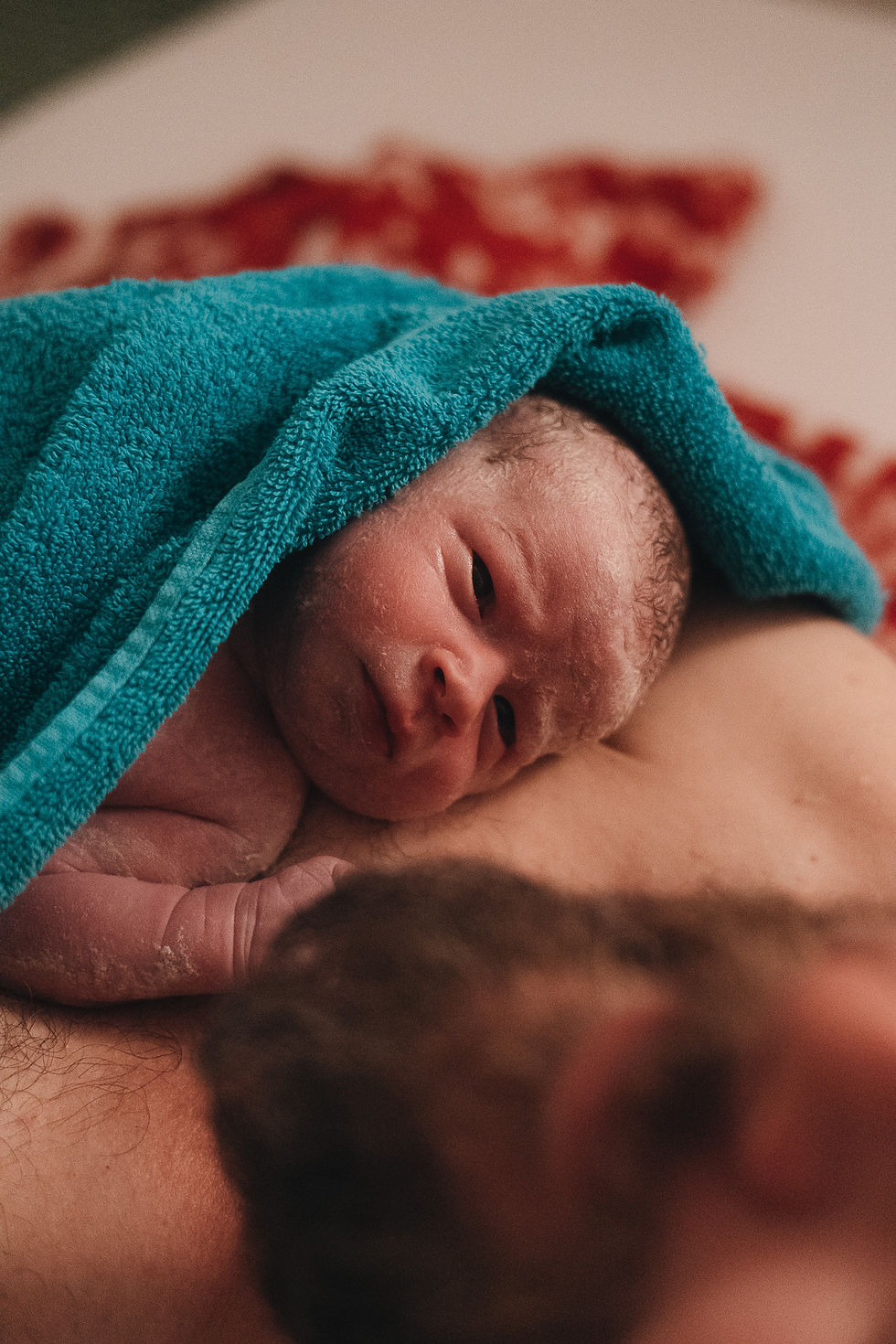 Neugeborenes Baby liegt direkt nach der Geburt auf der Brust des Vaters und blickt in die Kamera