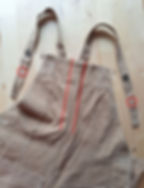 This image shows the top half of a pair of khaki Women’s Land Army dungarees, against a plain wooden background. Two red lines encase two parallel lines of unpicked stitching along the front seam bodice. A red circle indicates on each strap the unpicked sticking and original position of the buttons used to fasten the garment.
