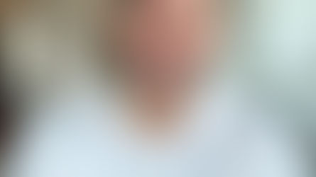 Smiling man in a white polo shirt with folded arms, in a bright room with white walls and cabinets, exuding a cheerful and welcoming mood.