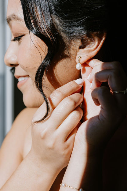 Bride putting on pearl drop earrings during wedding preparations at Saphire Estate.