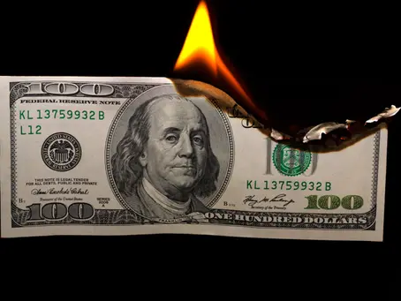 A US $100 bill burning against a black background, with flames consuming the upper right corner of the note.