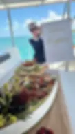 Captain Tanya in navy uniform holding a custom "Birthday Regina"
Pirates of the Caribbean welcome sign on a private yacht in Cancun, with a luxury
charcuterie and fruit display in the foreground.
