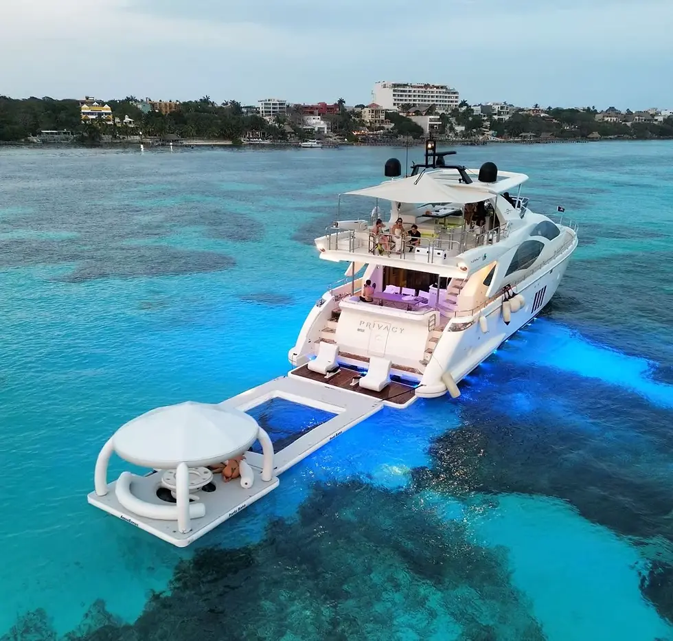 A luxury private yacht rental in Cancun glowing with blue
underwater lights, featuring an inflatable floating lounge platform with guests relaxing on
tropical water.