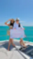 Captain Tanya in uniform sitting on the top deck flybridge of a
private Cancun yacht rental with a guest, holding a personalized welcome sign
against crystal-clear blue waters.