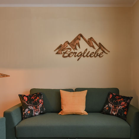 Grünes Sofa mit Kissen unter dem hölzernen Bergliebe Schild an der Wand im Apartment Sonthofen