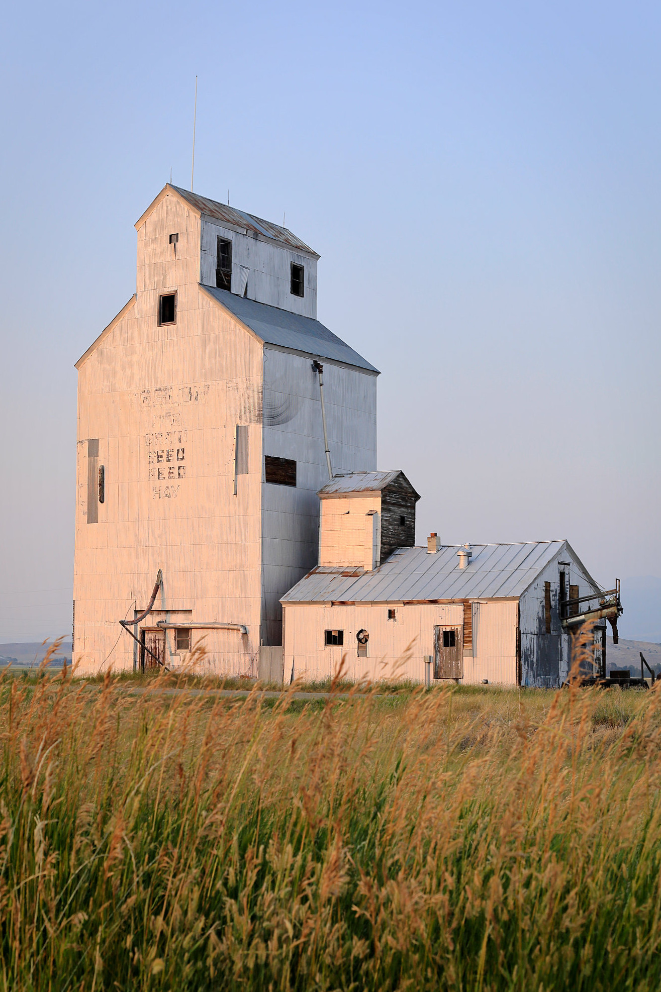 Warm and soft evening light hits the front of a grain elevator in Montana, as evening approaches.